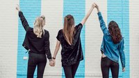 Drei junge Frauen machen Siegeszeichen vor einer Mauer